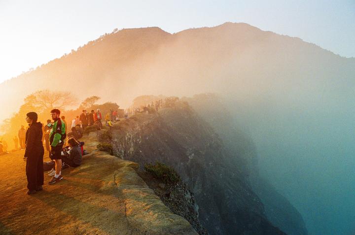 A group of people stand on a mountain ridge overlooking a valley filled with fog during sunrise.
