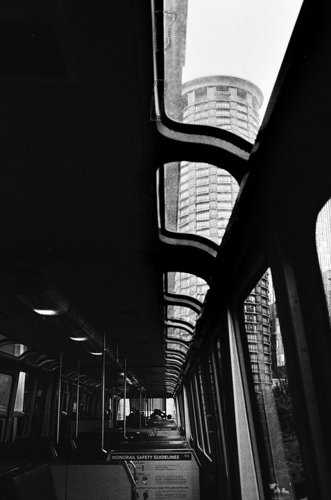 A monorail car interior is visible on the left, with a view of tall buildings outside the windows on the right.