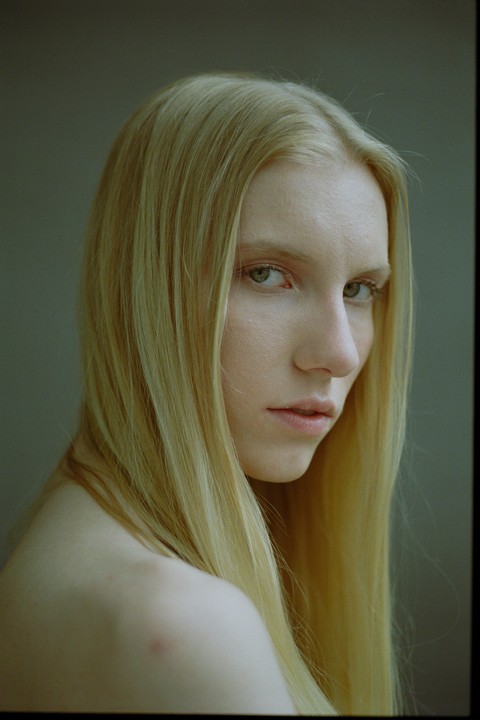 A woman with long blonde hair looks over her shoulder at the viewer.