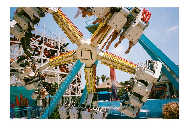 People are riding a spinning amusement park ride with a roller coaster in the background.