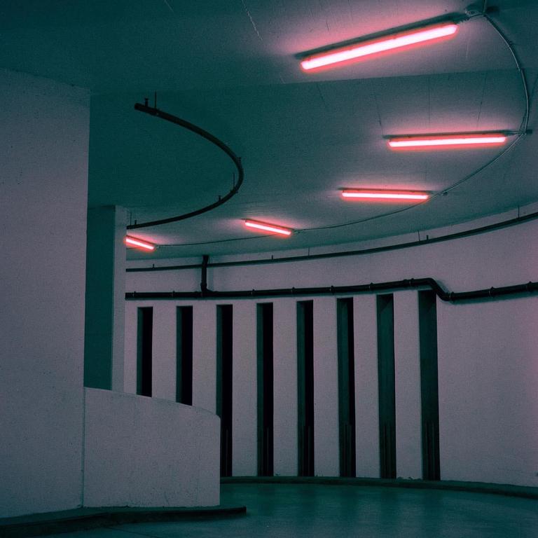 A parking lot with red neon lights on the ceiling and a curved wall.