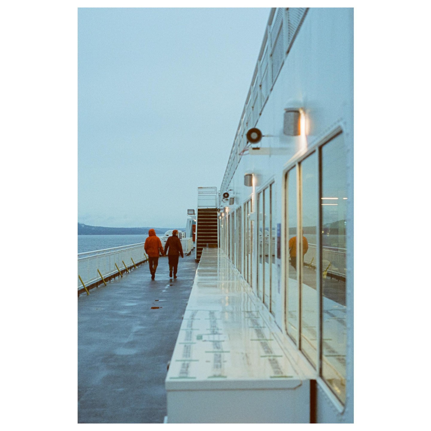 A couple walks hand-in-hand on the deck of a ferry boat on a cloudy day.