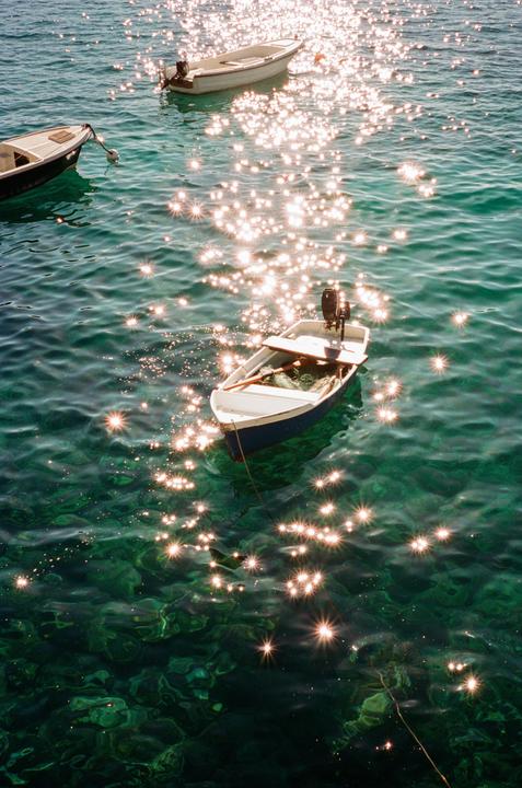 Three small boats float on sparkling green water.