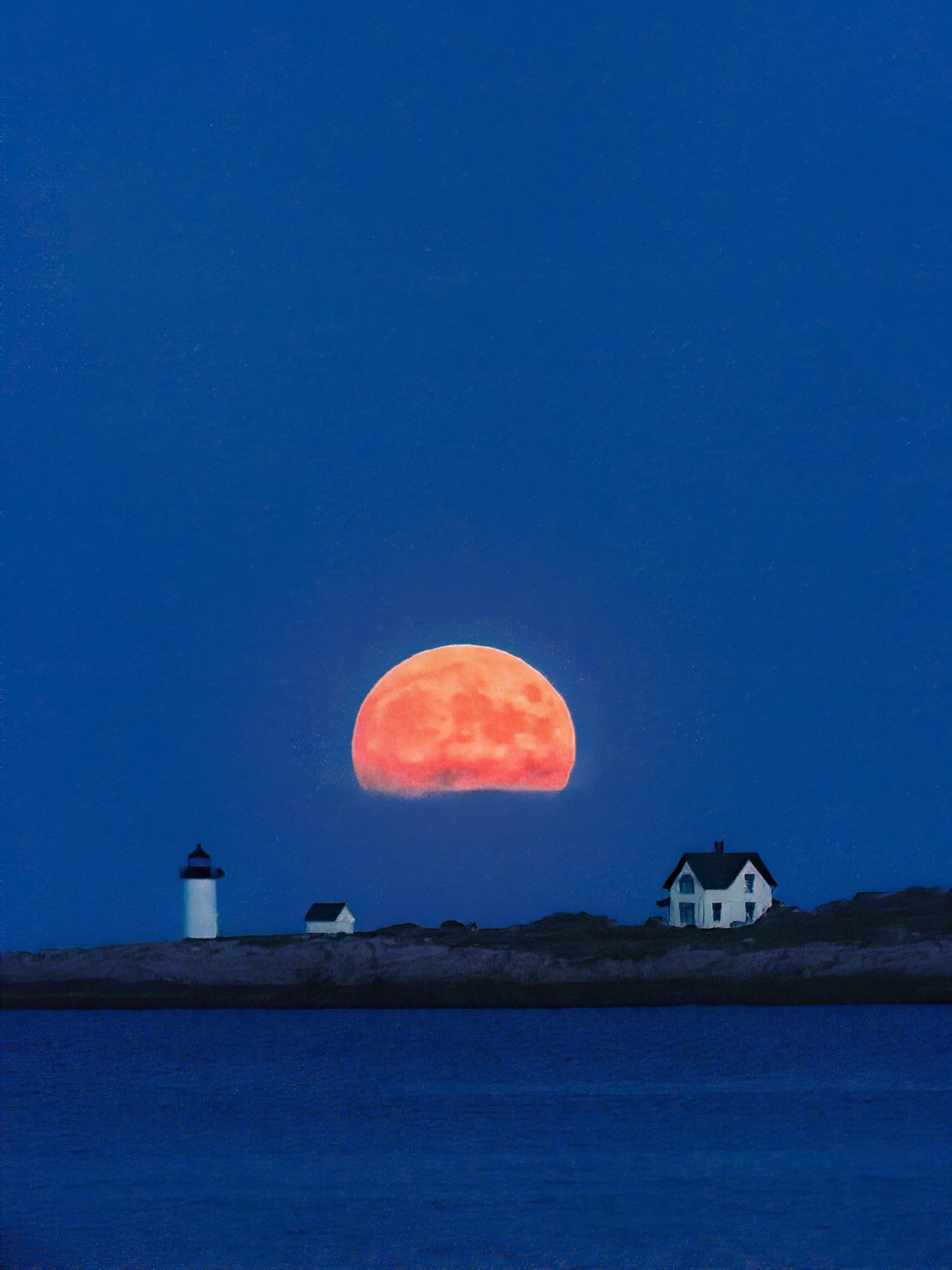 A large orange moon rises over a body of water with a lighthouse and houses on the distant shore.