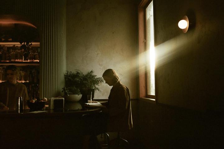 A person sits at a bar counter, illuminated by a beam of light from a window.