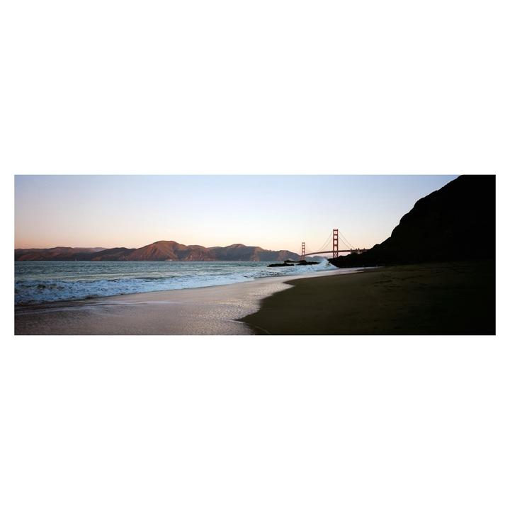 A panoramic view of a beach with waves crashing on the shore, mountains in the distance, and the Golden Gate Bridge.