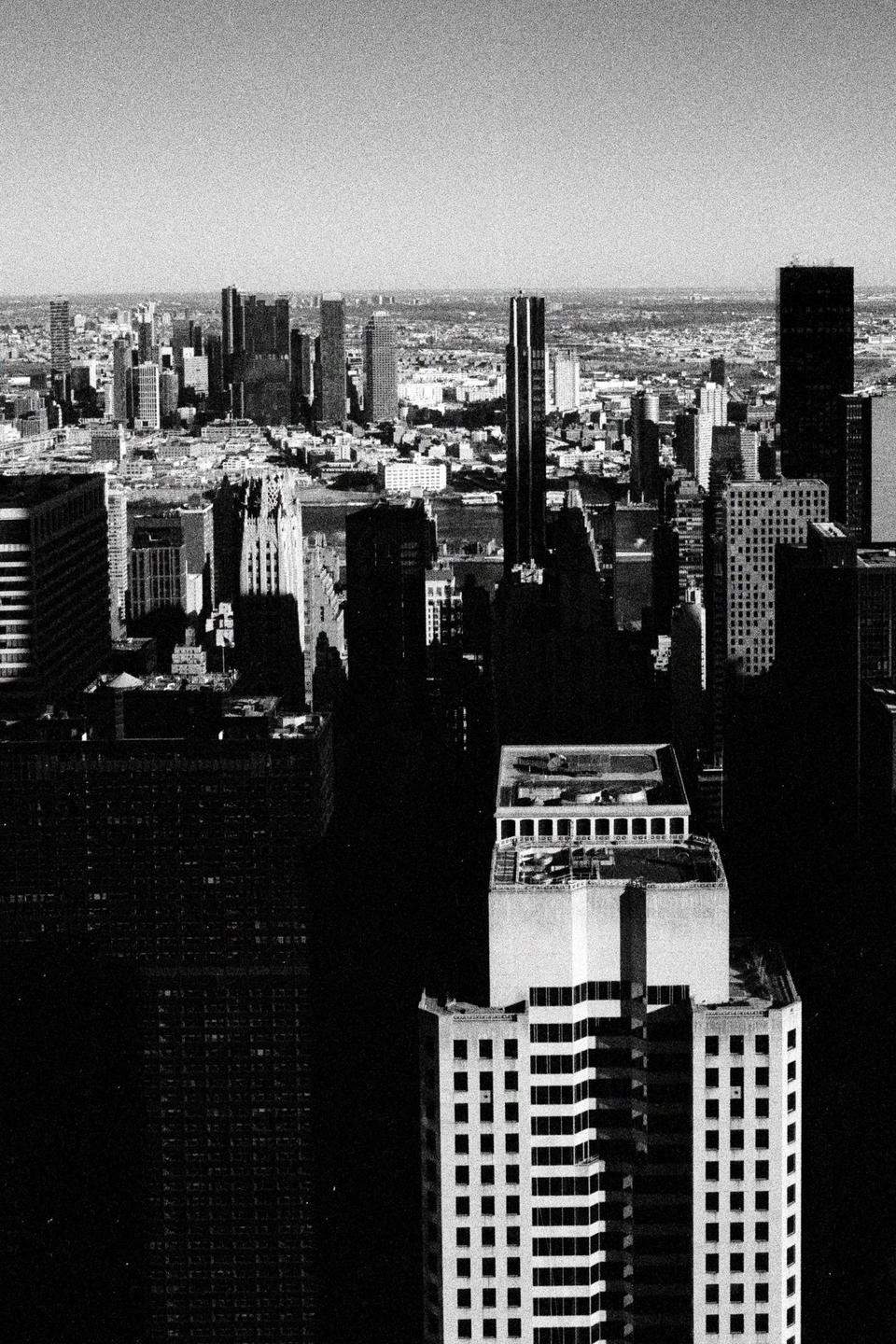A high-angle black and white view shows a city skyline with many tall buildings and a river in the distance.