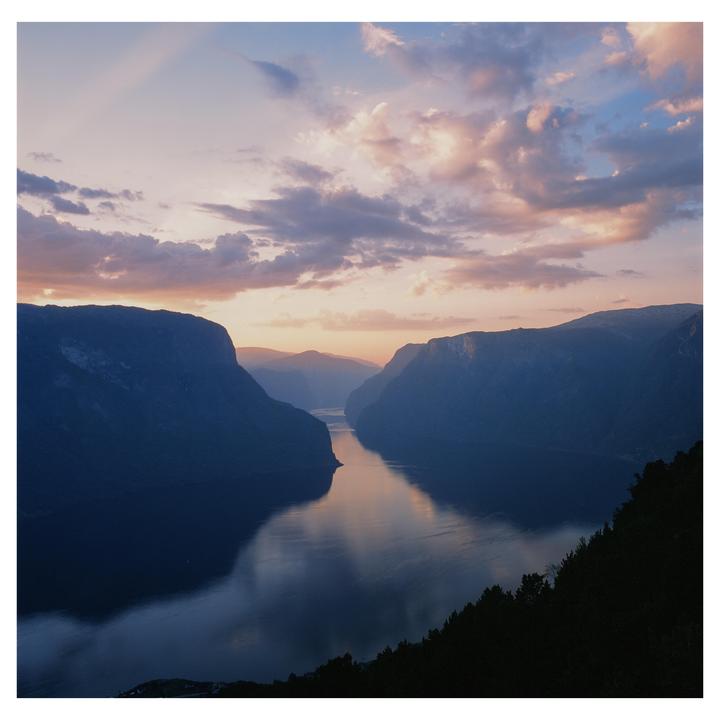 A wide body of water reflects the sunset sky between two large mountains.