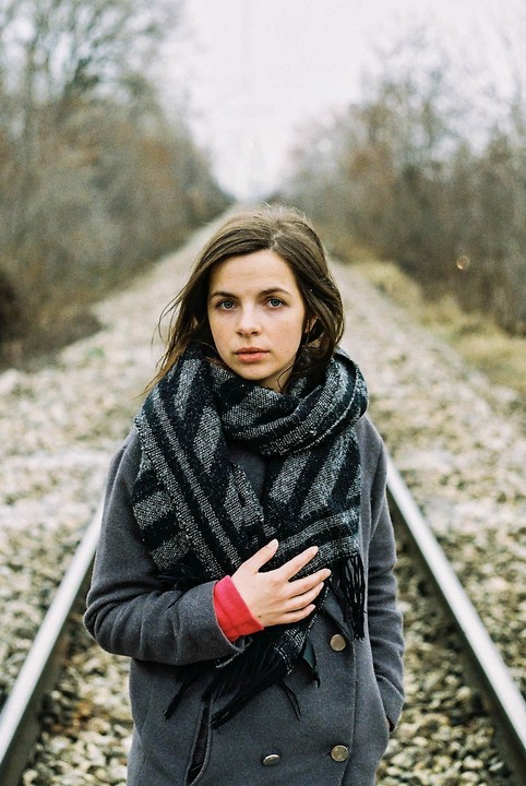 A woman wearing a scarf and coat stands on a railway track.