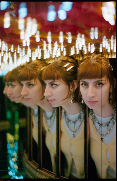 A woman with red hair and bangs is reflected multiple times in a funhouse mirror.