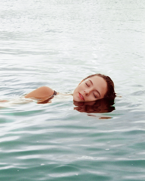 A woman with her eyes closed floats on her back in the water.