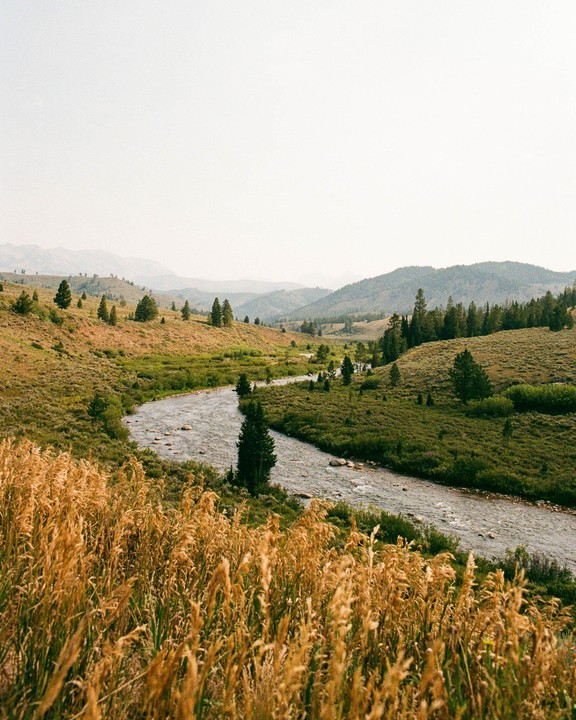 A river winds through a valley with hills and trees under a hazy sky.