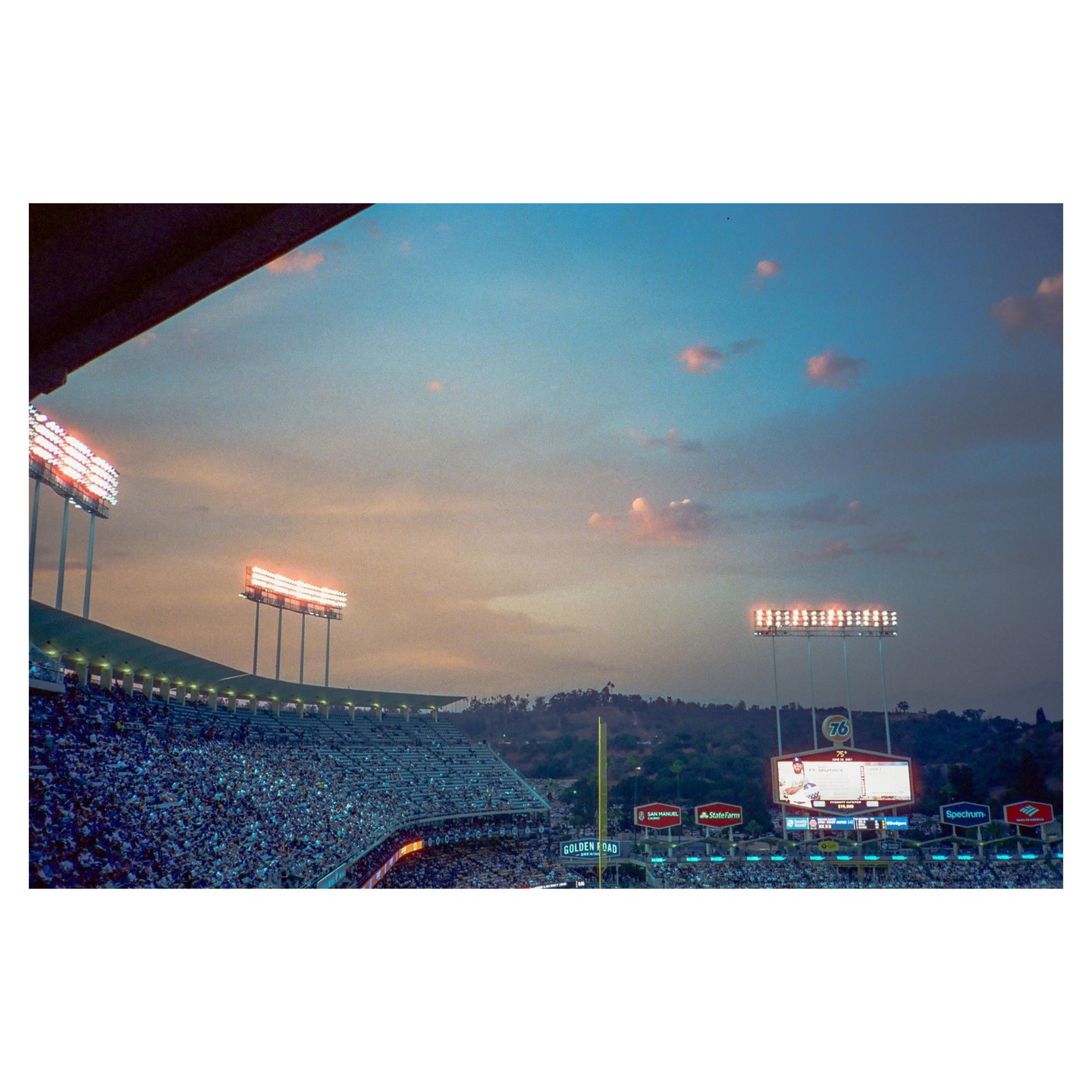 A baseball stadium is filled with spectators under a colorful sky at dusk.