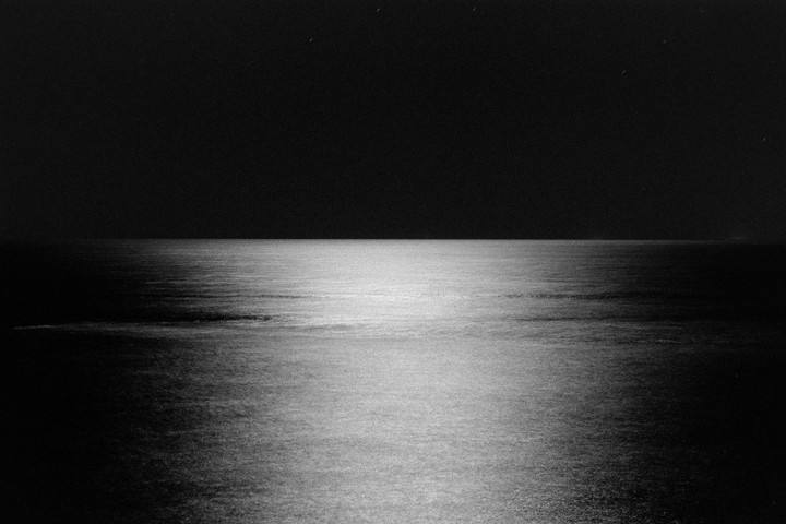 The ocean reflects light from the sky at night, with a few stars visible above the horizon.