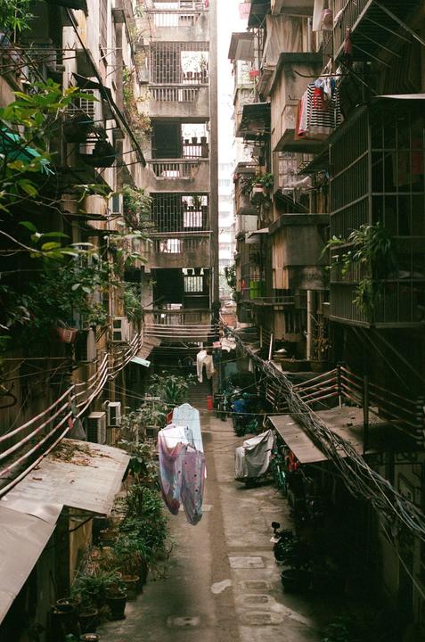 Laundry hangs to dry in a narrow alley between two tall, weathered buildings.
