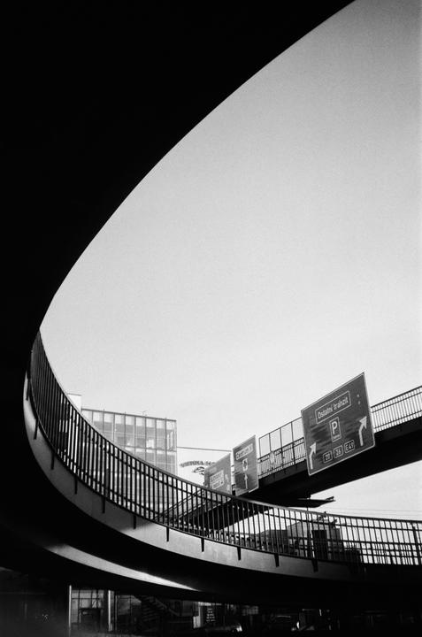 A curved pedestrian bridge with railings and street signs is visible against a bright sky.