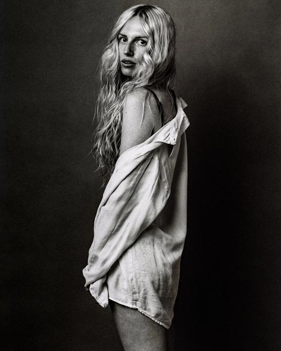 A woman with long, wavy hair looks over her shoulder while wearing an unbuttoned shirt.