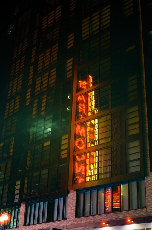 A tall building with many windows reflects a neon sign at night.