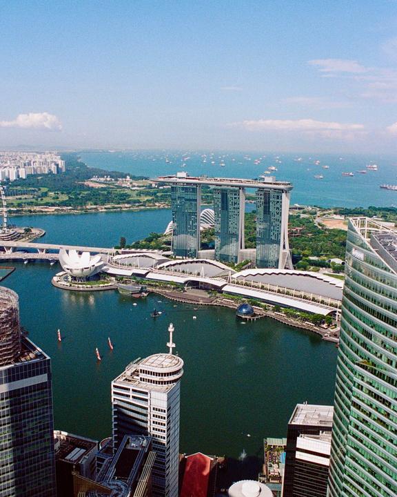 A high-angle view shows a city skyline with a large body of water and many ships in the distance.