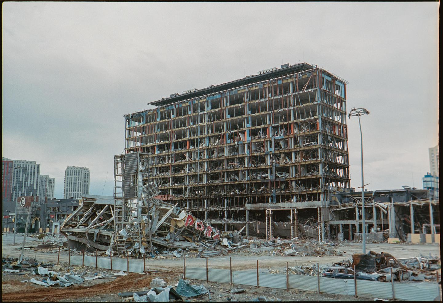 A large, multi-story building stands severely damaged with its interior exposed and debris scattered around it.