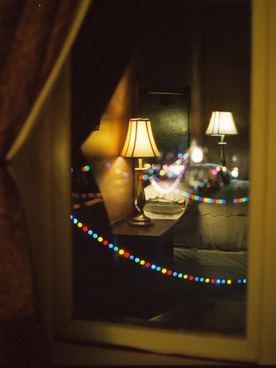 Two lamps illuminate a room with colorful string lights reflected in a window.