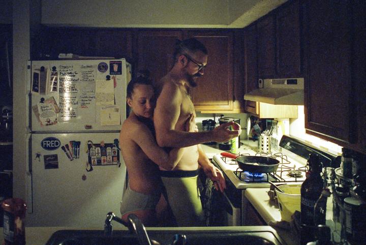 A couple embraces in a kitchen while cooking on a gas stove.