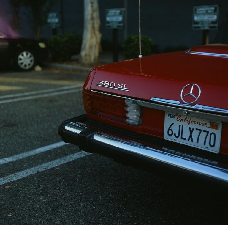 The rear of a red Mercedes 380 SL with a California license plate is parked on asphalt.