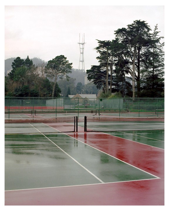 Rain-slicked tennis courts are visible in the foreground, with a tall transmission tower on a hill in the background.