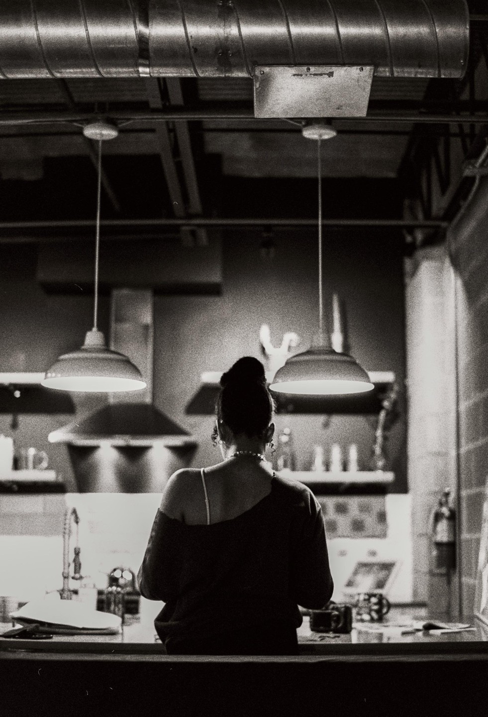A woman with her back to the viewer stands in a kitchen under two pendant lights.