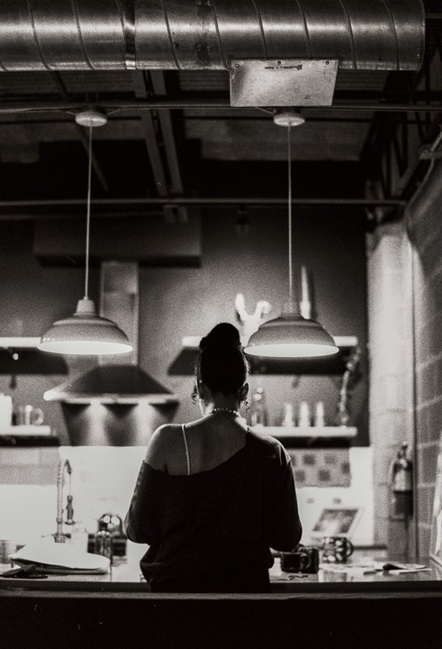 A woman with her back to the viewer stands in a kitchen under two pendant lights.