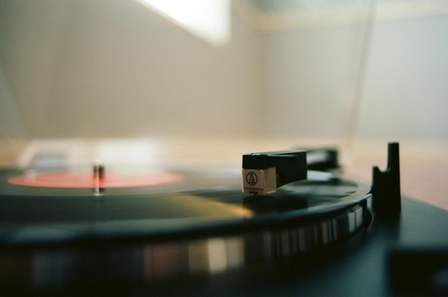 A record player with a red label record is shown in a close-up shot.