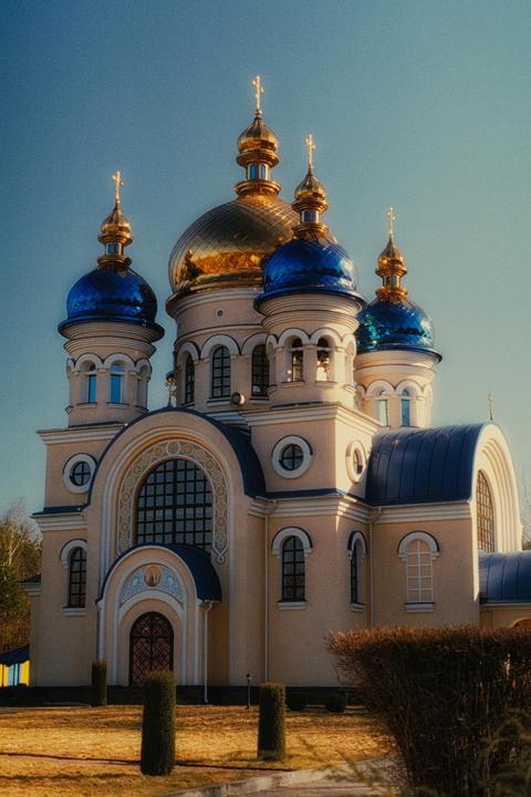 A large church with golden and blue domes stands against a clear blue sky.