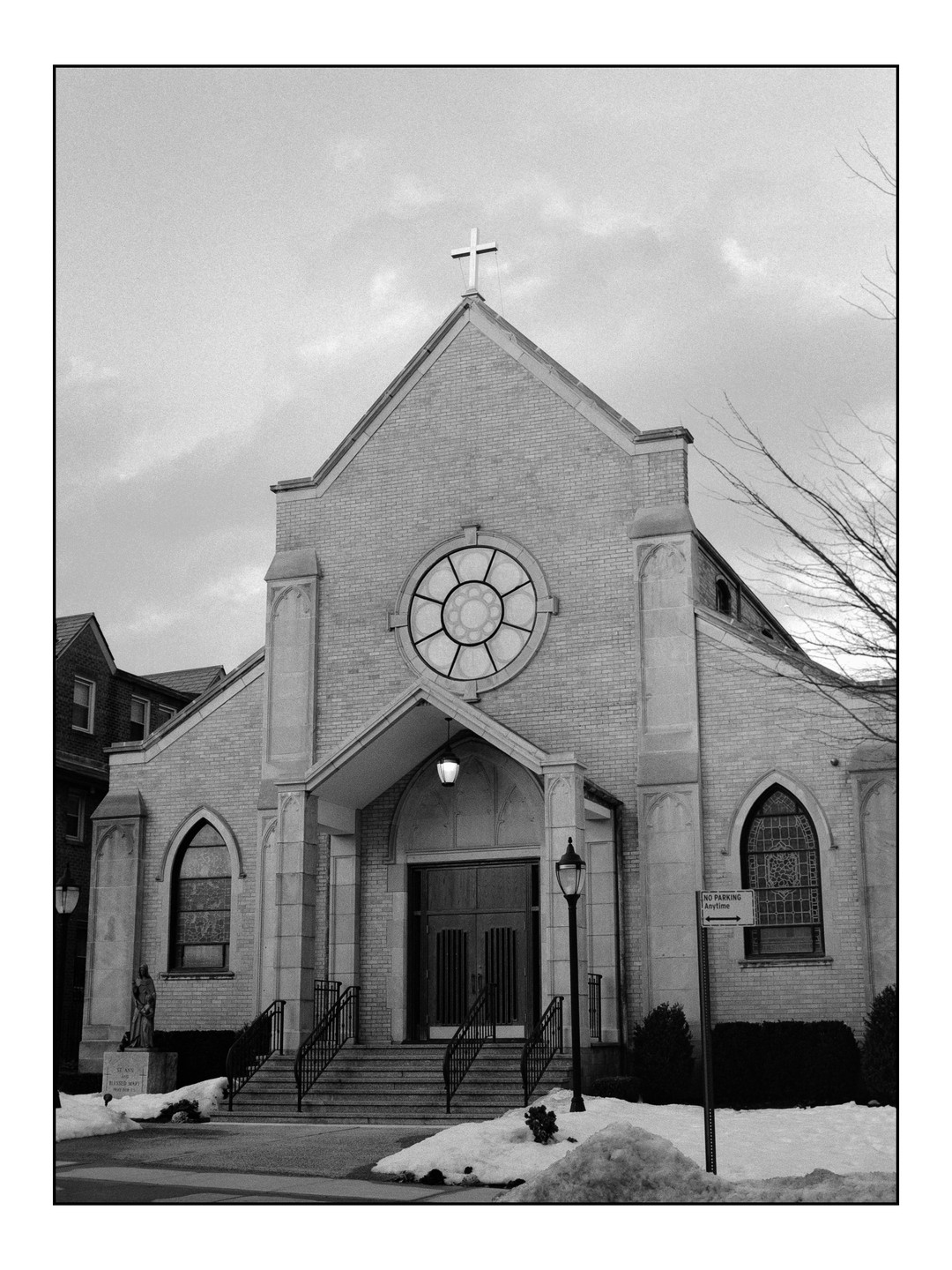 A church with a cross on its roof stands in front of a cloudy sky, with snow on the ground.