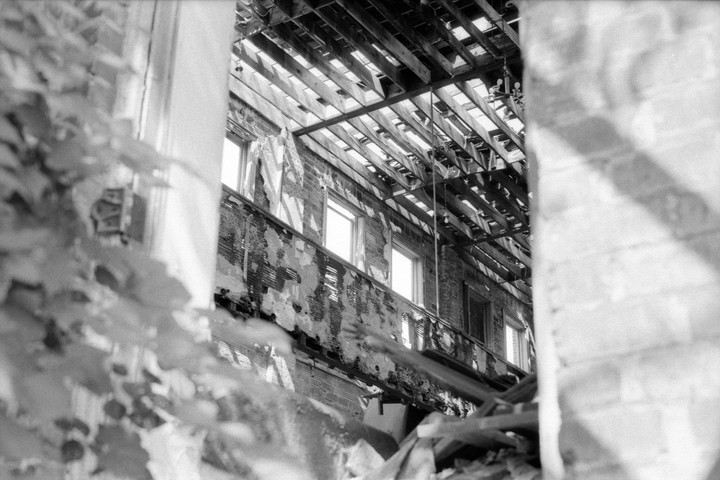 A view through a window shows the interior of an abandoned building with a collapsed roof and exposed wooden beams.