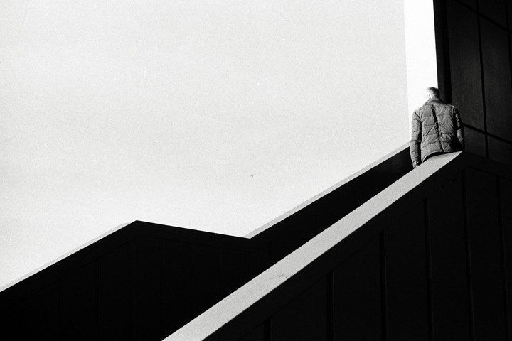 A man stands at the top of a dark, angular structure against a bright sky.