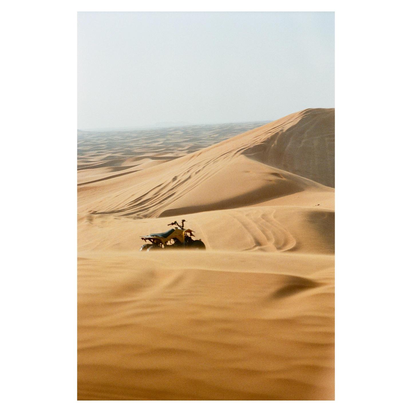 An all-terrain vehicle is parked on a sand dune in a desert landscape.