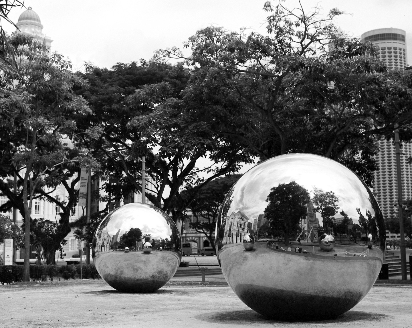 Two large, reflective spheres sit on the ground in a park-like setting with trees and buildings in the background.