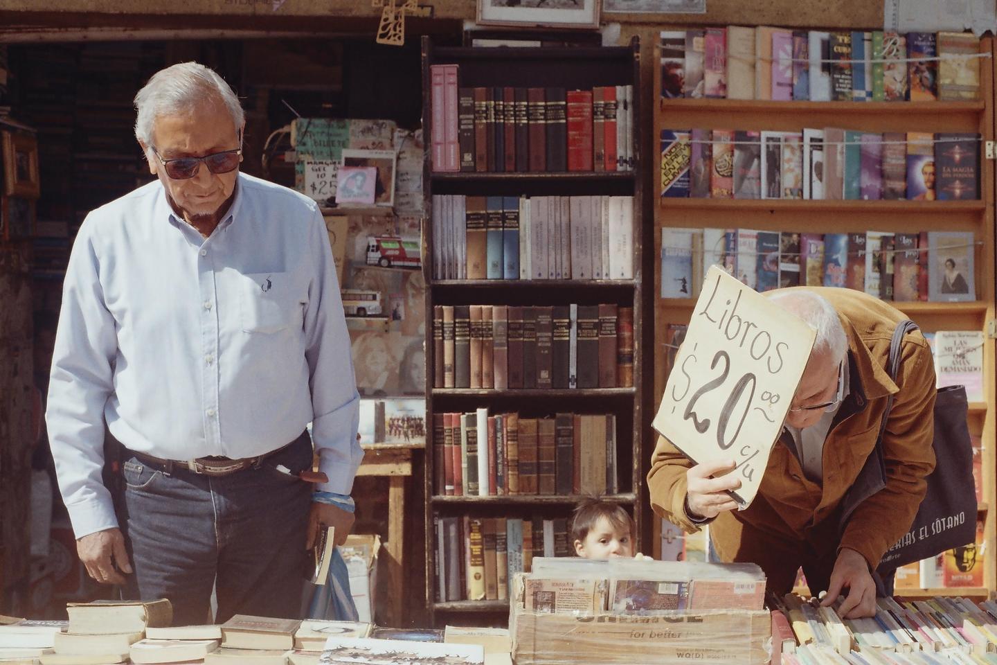 Two men and a child are looking at books in an outdoor book stall.