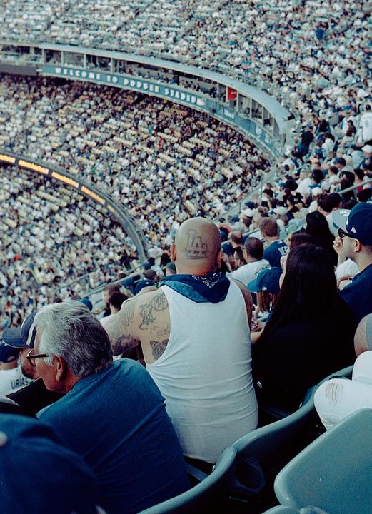 A man with a shaved head and tattoos on his arms sits in a stadium full of people.