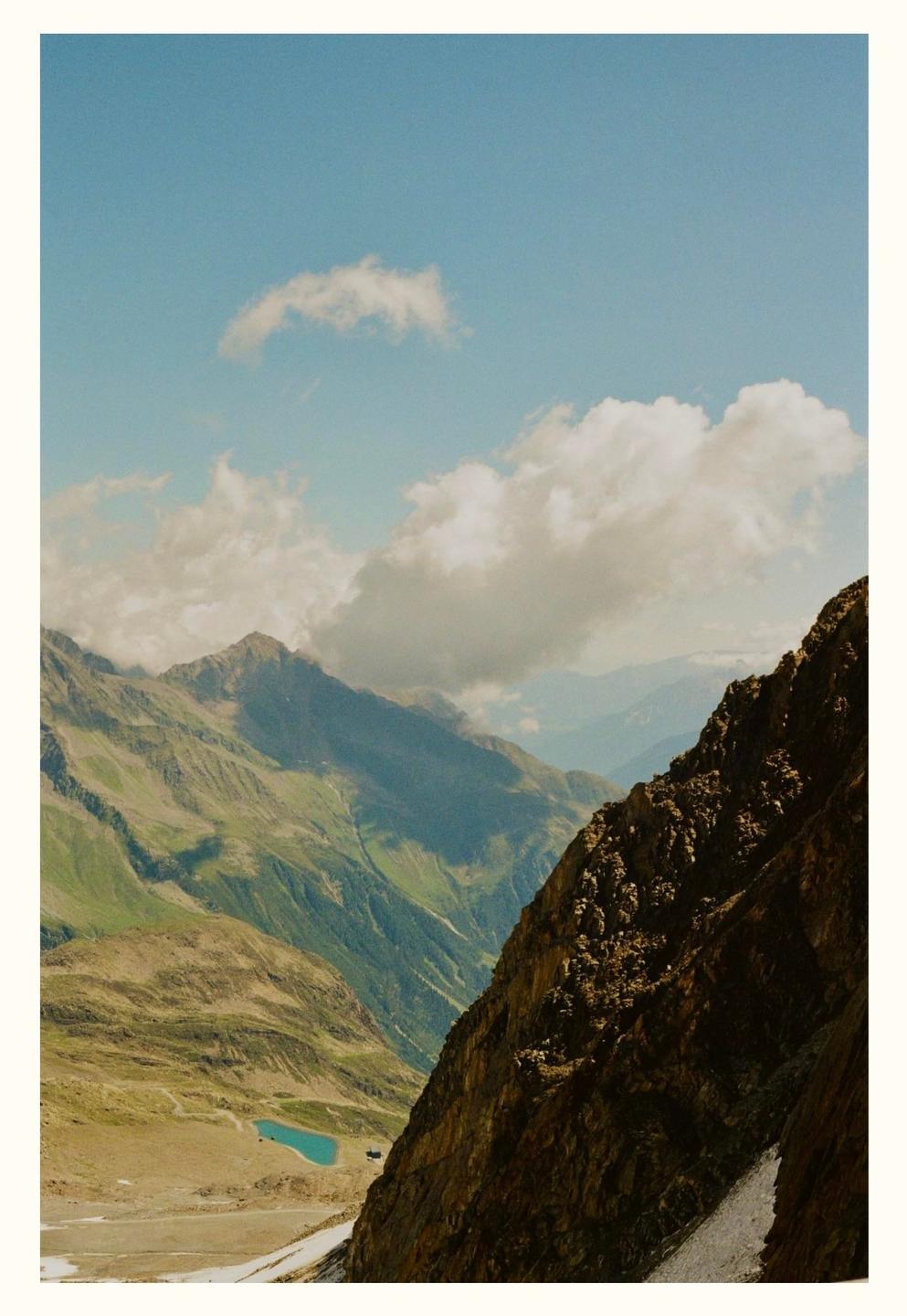 A steep, rocky mountain face dominates the right side of the frame, with a valley and distant green mountains under a cloudy sky.