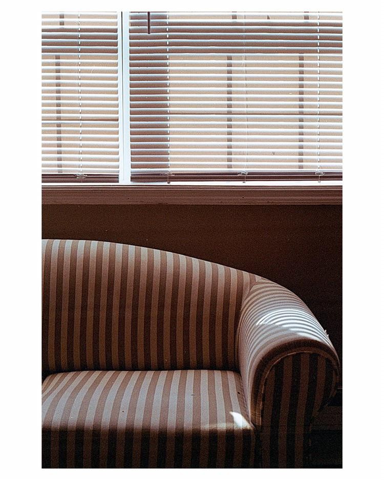 Sunlight streams through window blinds, casting striped shadows on a striped sofa.