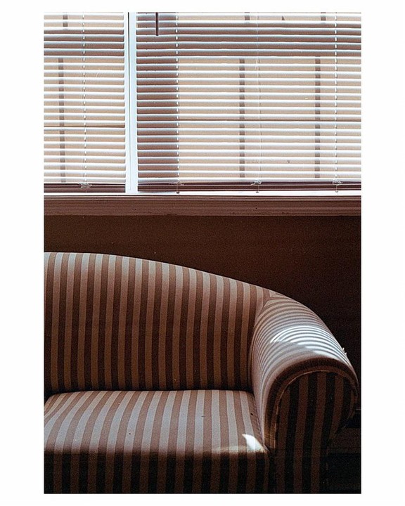 Sunlight streams through window blinds, casting striped shadows on a striped sofa.