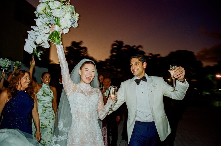 A bride and groom celebrate with champagne and flowers, surrounded by guests at dusk.