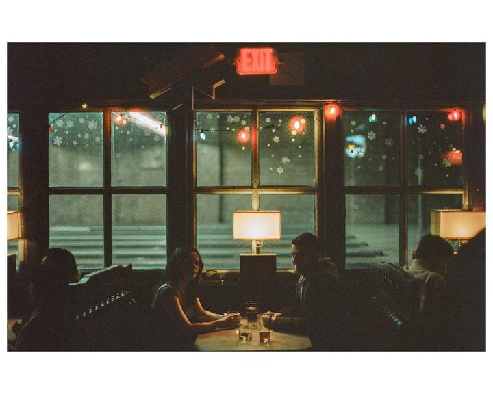 A couple sits at a table in a dimly lit restaurant with snowflake decals and string lights on the window.