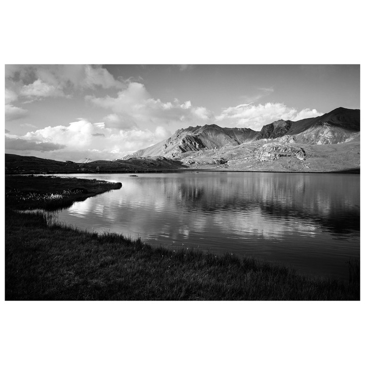 A lake reflects mountains and clouds under a bright sky.