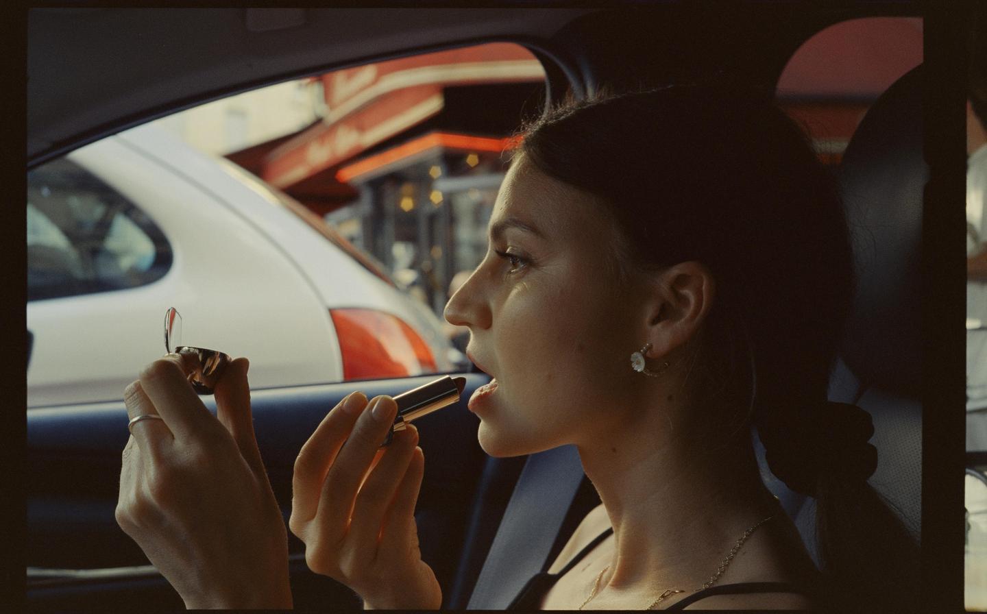 A woman applies lipstick while sitting in a car.