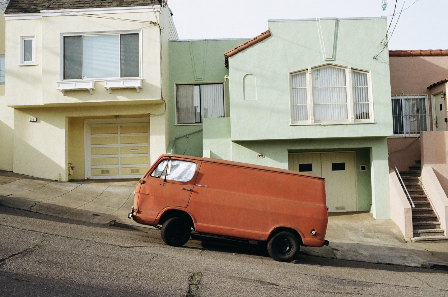 An orange van is parked on a steep street in front of three houses.