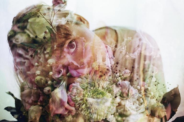 A woman's face is visible through a double exposure with flowers and foliage.
