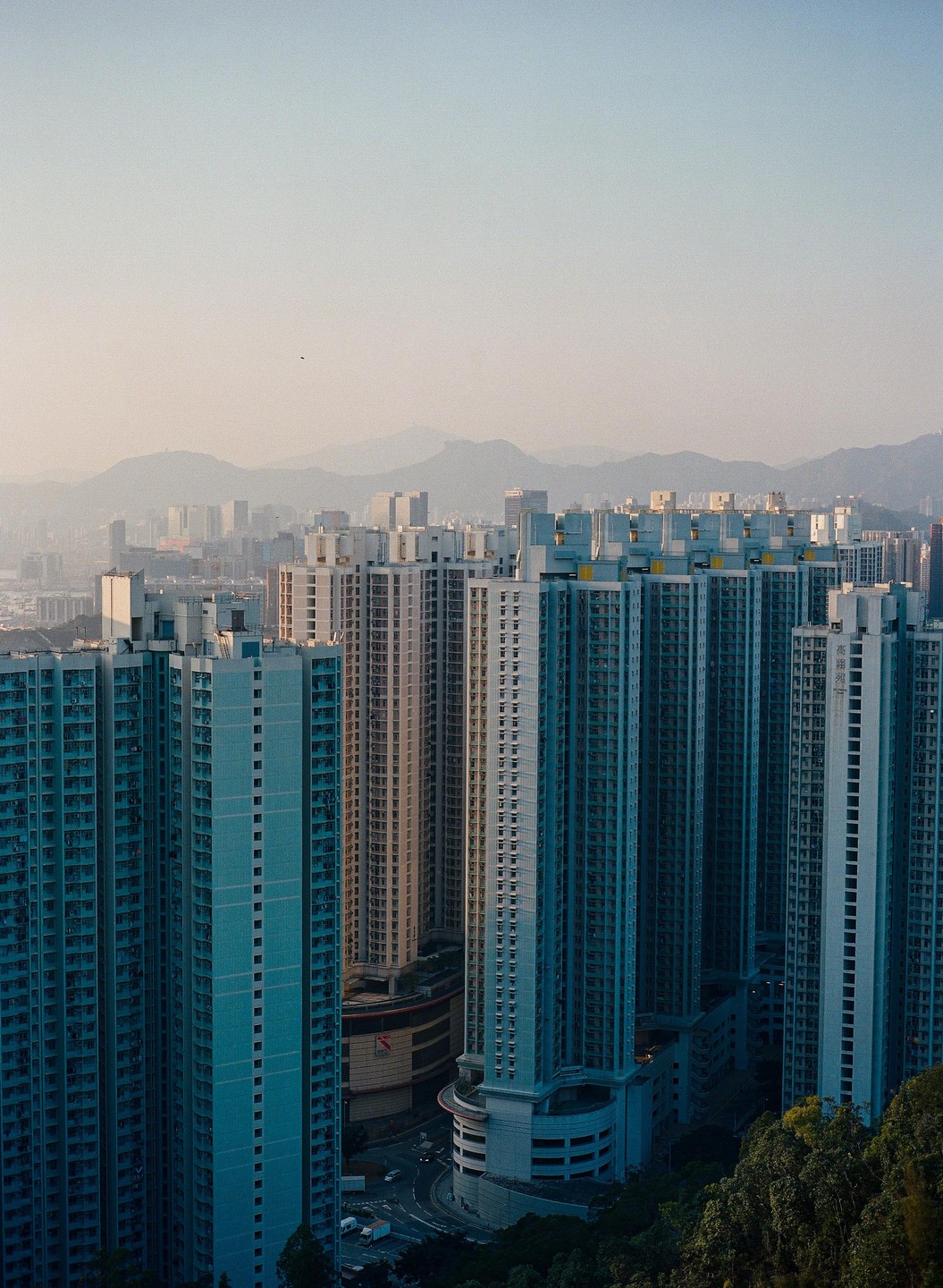 A dense urban landscape of tall residential buildings with mountains in the hazy background.