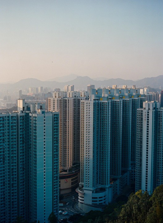 A dense urban landscape of tall residential buildings with mountains in the hazy background.